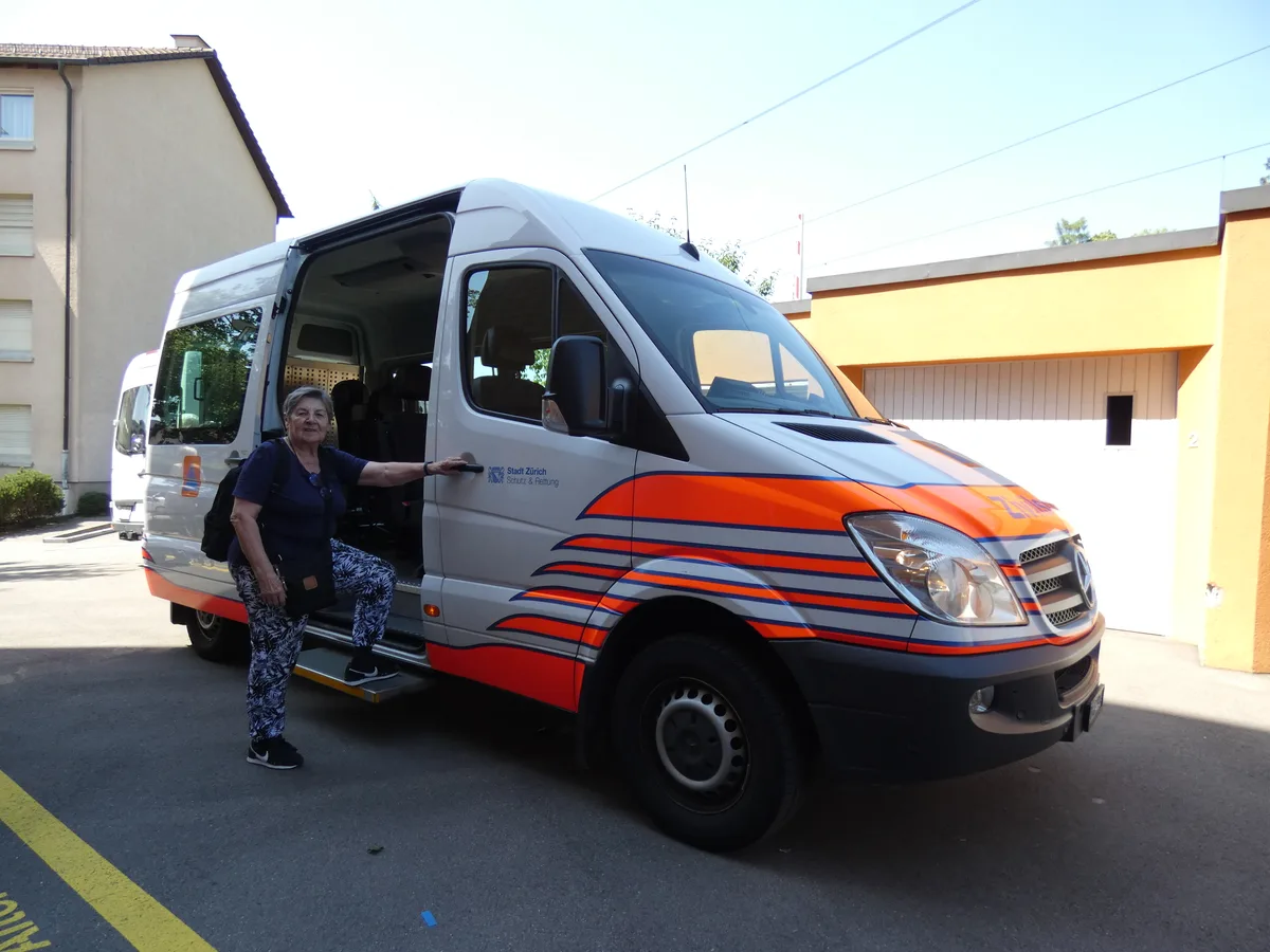 Frau Maurer wird von einem Transporter abgeholt.